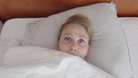 close-up of a woman lying in bed, suddenly opening her eyes wide in shock. her startled facial expression reflects fear, surprise or a bad dream