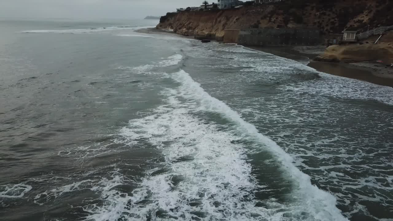 vista de un avión no tripulado volando de vuelta sobre la costa mostrando la playa, algunas casas y el océano