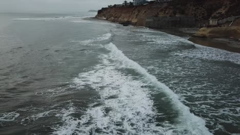 view from a drone flying back over the coast showing the beach, some houses and the ocean