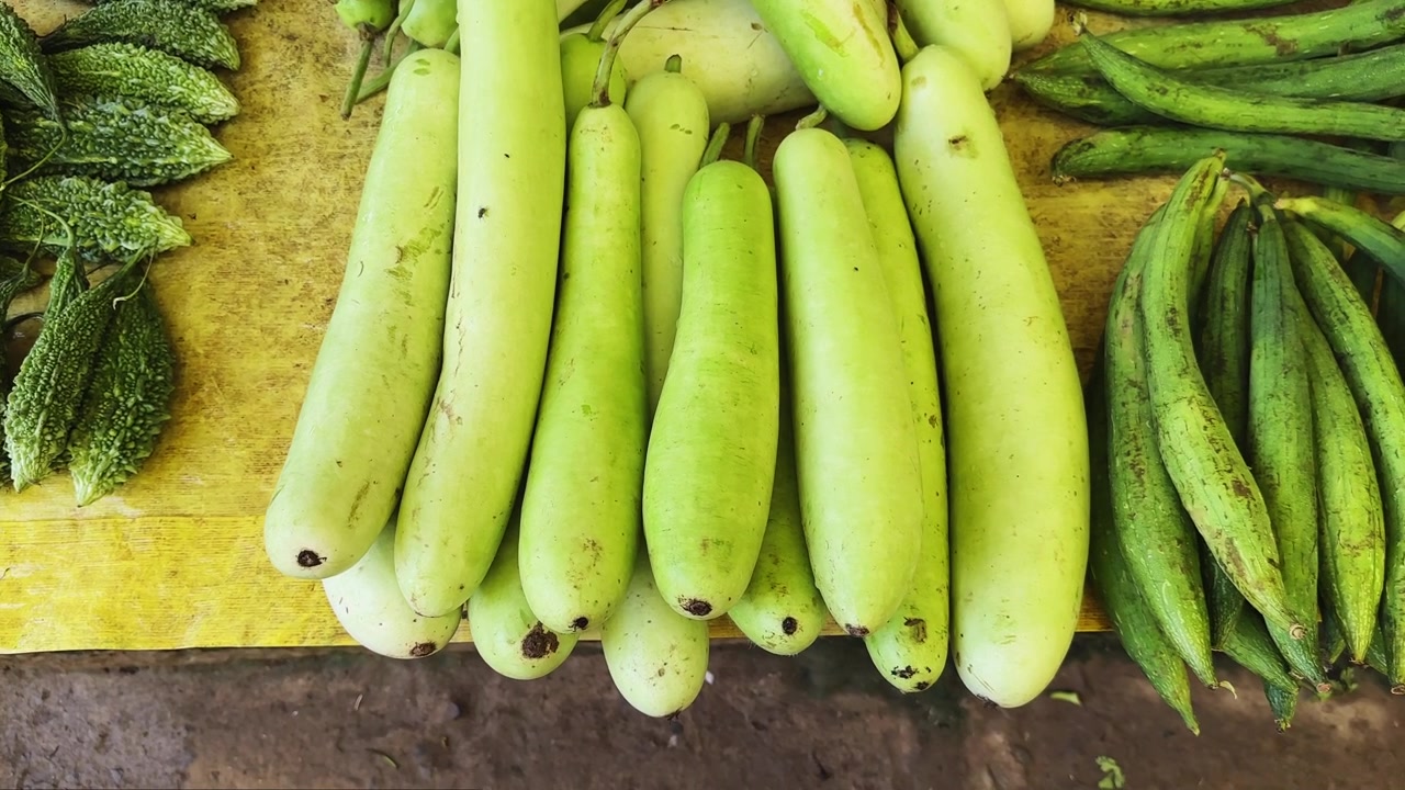 Ujęcie z jazdy przez lokalny stragan na targu, prezentujący świeże tykwy i gorzkie melony na sprzedaż.