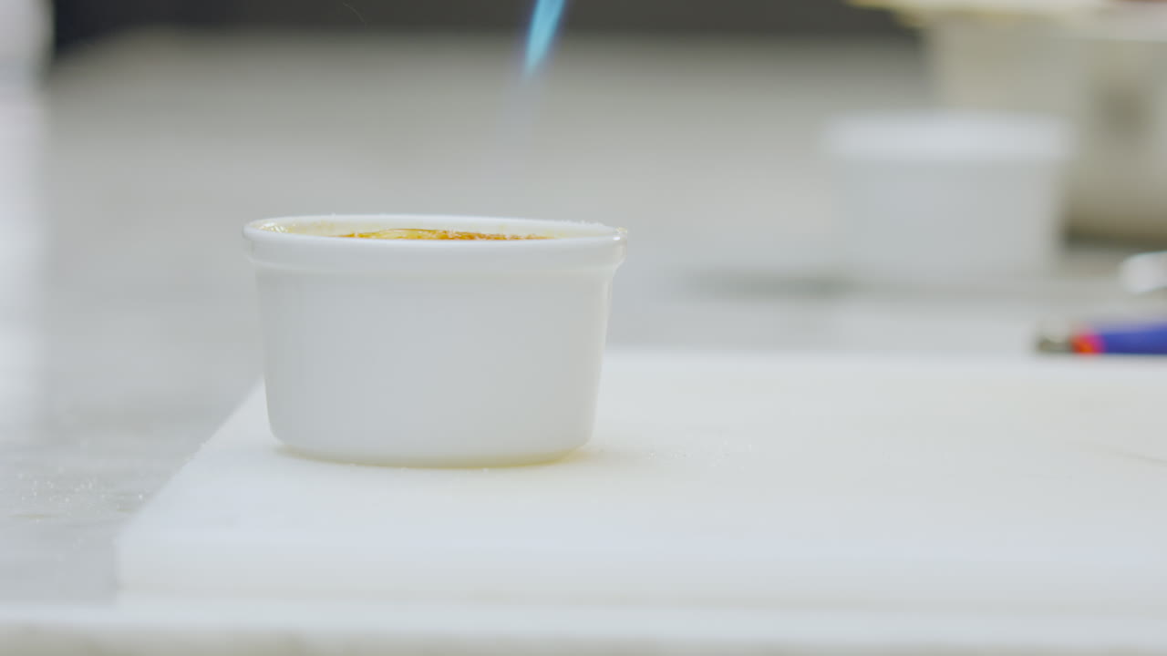 Close-up of a creamy dessert creme brulee served in a ceramic mold is torched to give it a golden color on a white counter