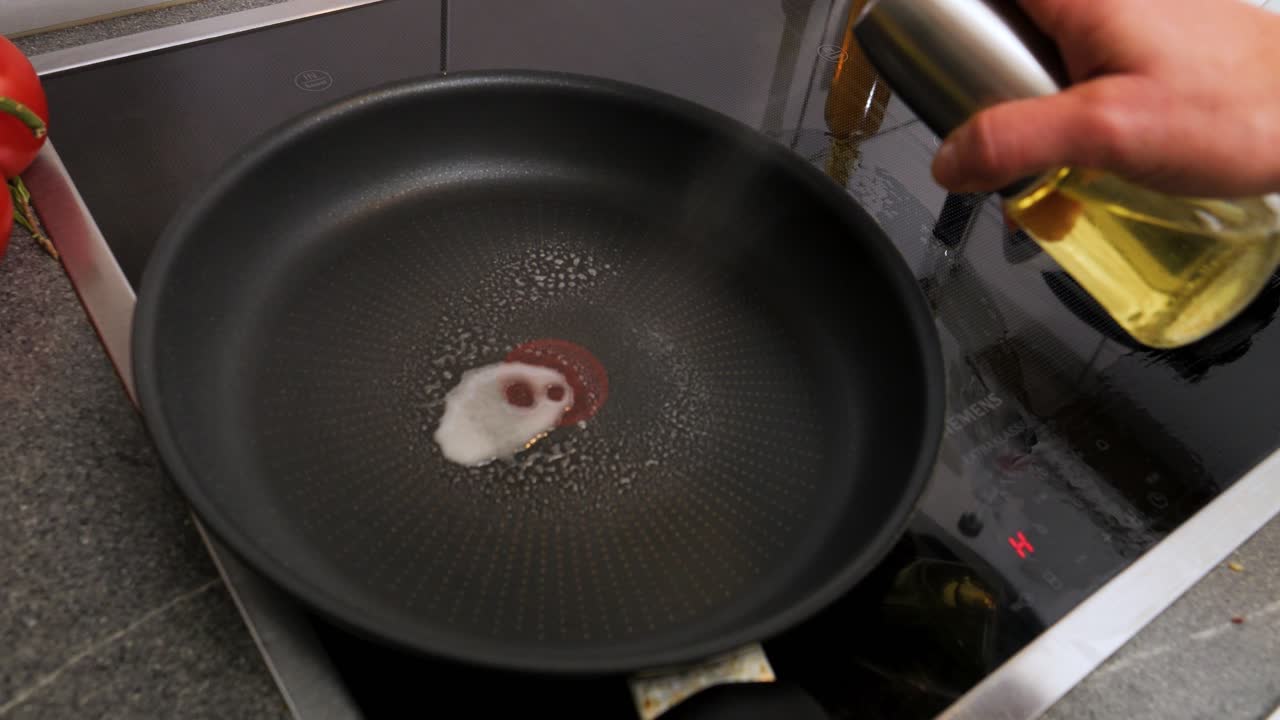 tiro medio lento de un rociador de aceite lleno de aceite de oliva vegano mientras una mujer rocía la sartén caliente antes de cocinar para una deliciosa cena en la cocina a cámara lenta