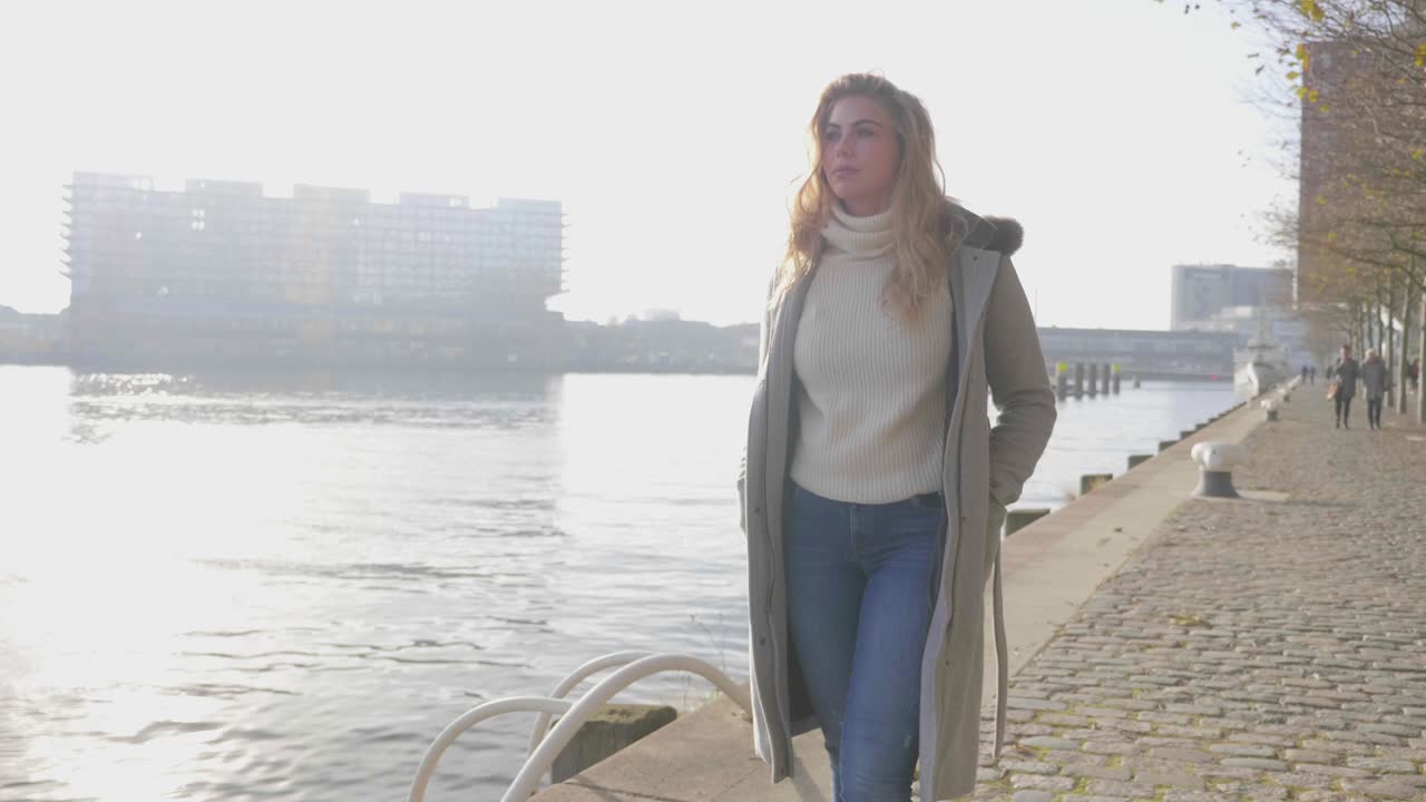 Nachdenkliche junge Frau geht in Zeitlupe einen Pier entlang.