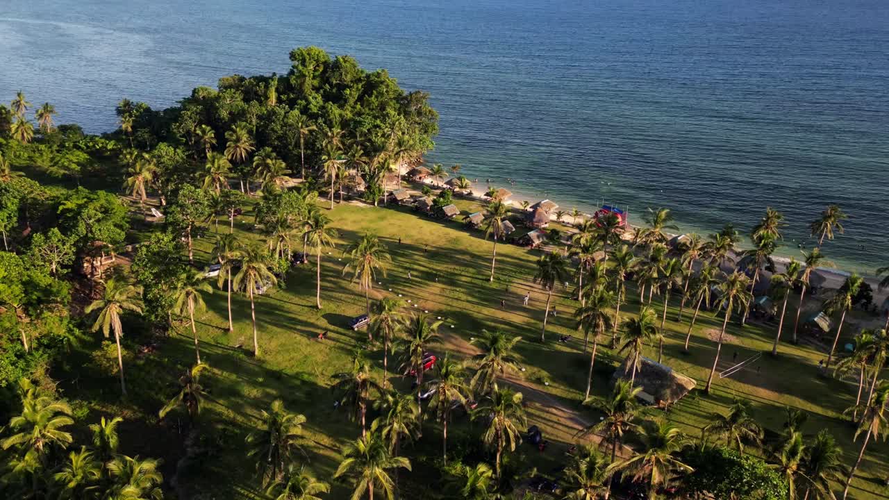 Vibrant aerial orbit hyperlapse of lush palm trees and coastline along a tropical island beach resort during sunset - Bagasbas, San Andres, Catanduanes, Philippines.