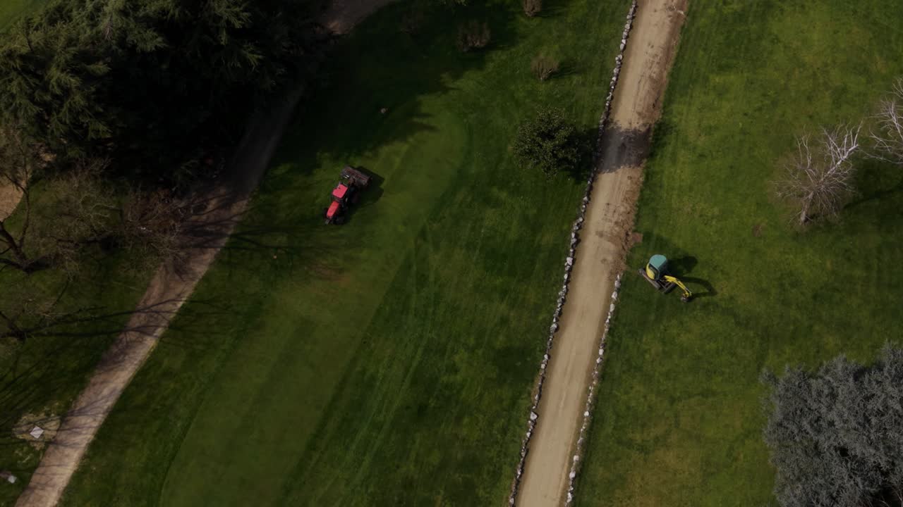 Ripresa drone di attrezzature di manutenzione al lavoro su un campo da golf, che preparano superfici verdi lisce per sport e svago.