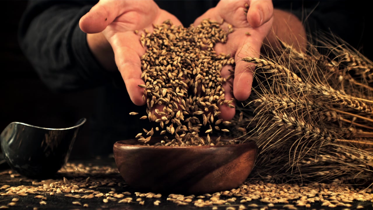 Hands Pouring Golden Wheat Grain into a Wooden Bowl in Slow Motion