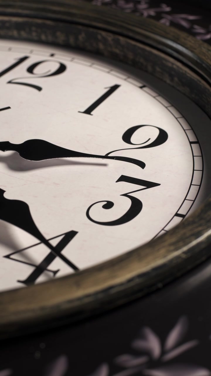 Primo piano verticale del quadrante di un orologio analogico vintage. Le lancette dell'orologio girano rapidamente in senso orario oltre i numeri uno, due e tre mentre le ombre si muovono sul quadrante. Ripresa macro timelapse statica.