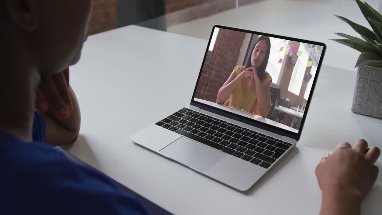 African american businesswoman sitting at desk using laptop having video call with female colleague