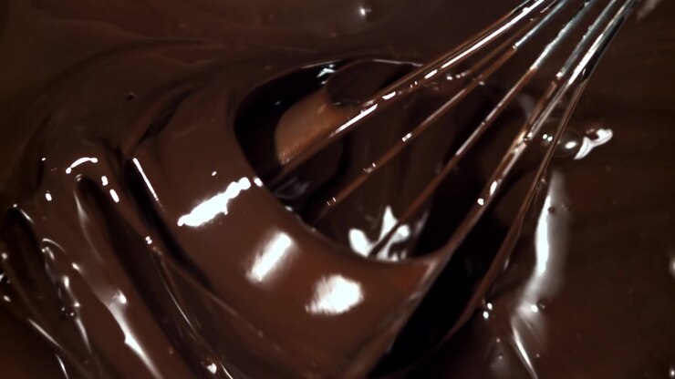Primo piano di una frusta che mescola cioccolato fondente fuso al rallentatore