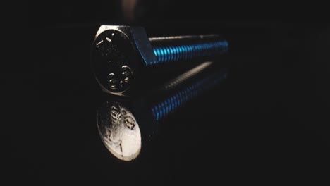 Macro-low-push-out-shot-of-a-metal-bolt-on-a-reflective-surface-with-a-black-background-using-a-probe-lens