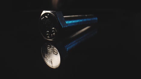 tiro de empuje bajo macro de un perno de metal en una superficie reflectante con un fondo negro usando una lente de sonda