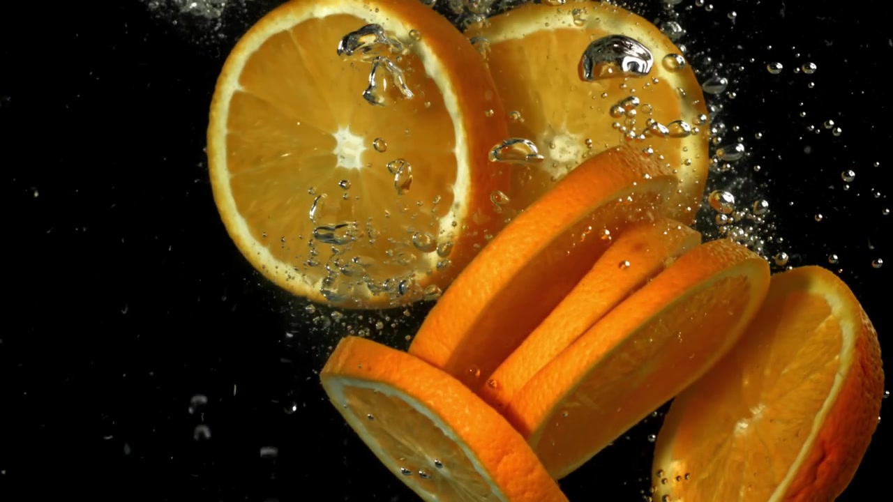 Fette d'arancia fresche che schizzano nell'acqua al rallentatore
