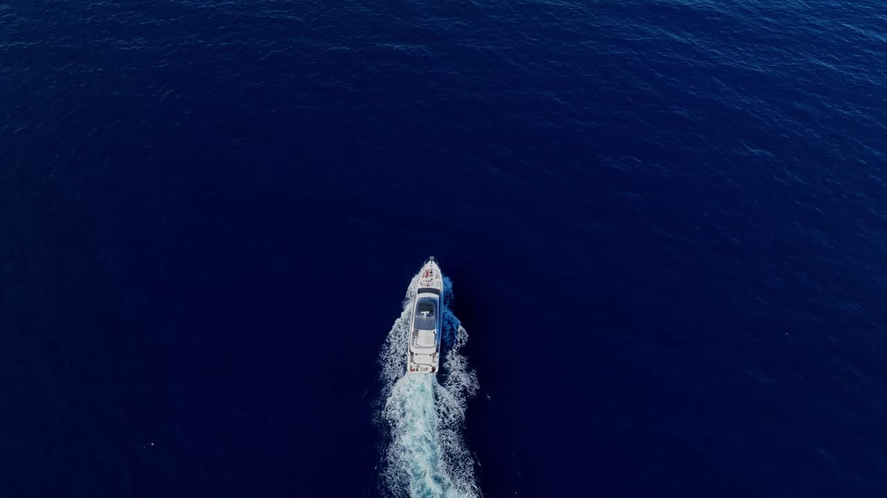 A single white boat cuts through dark blue open water in the Kornati archipelago, aerial top down tilt up in slow motion