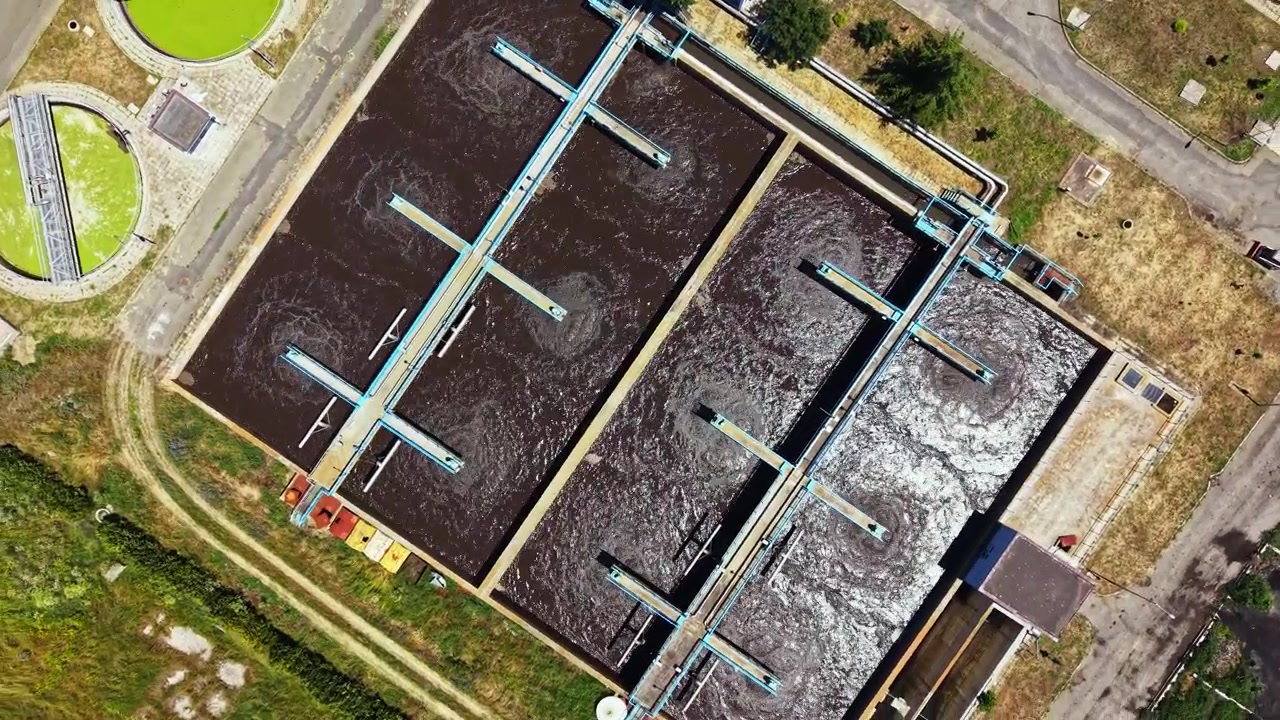 Water treatment facility in a rural area processes wastewater using large tanks and equipment during daylight hours under clear skies