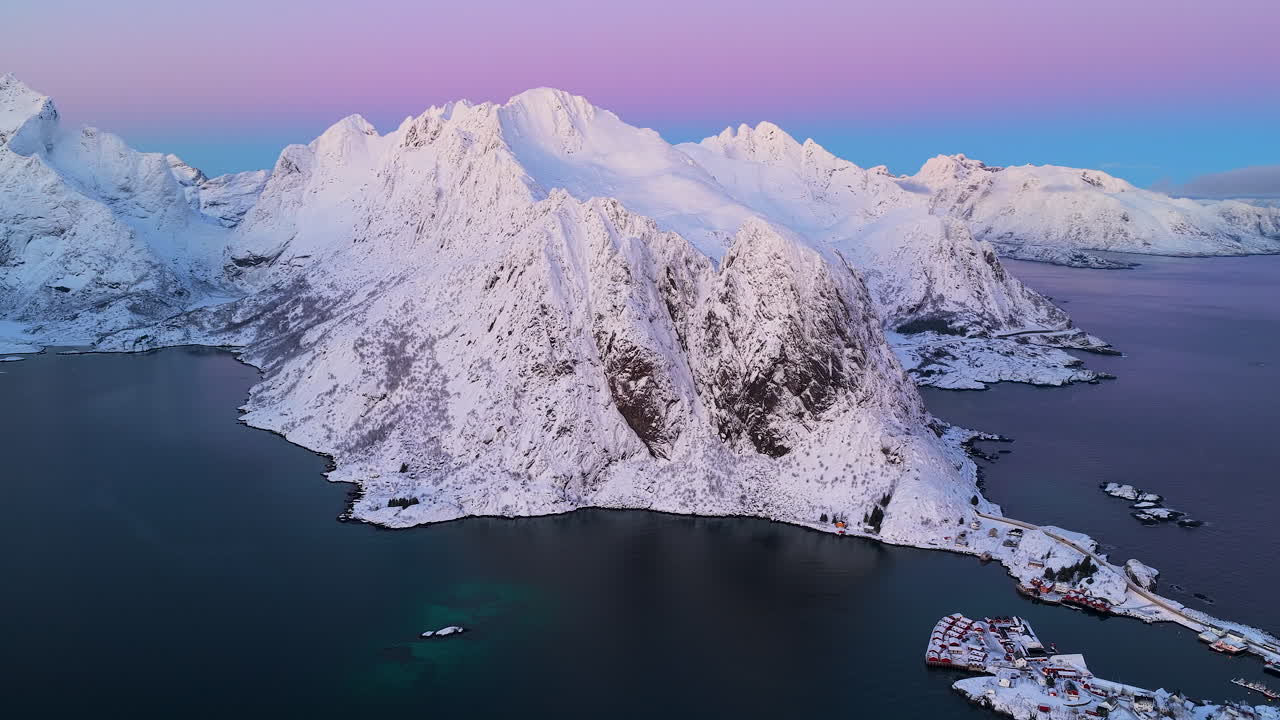 Henkeäsalpaava dronekuva lumisista norjalaisista huipuista ja vuonoista Lofootilla purppuranpunaisen auringonlaskun aikaan. Täydellinen matkadokumentteihin ja hyvinvointisisältöön.