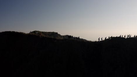 hikers at the summit of mout batur volcano in bali indonesia walk along the crater ridge, aerial orbit reveal shot