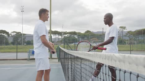 Happy-diverse-male-tennis-players-over-the-net-at-outdoor-tennis-court-in-slow-motion