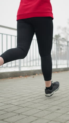 lower angle view of athlete in black sneakers and leggings jogging near iron railing of bridge in winter with visible breath vapor in foggy urban background conveying cold outdoor fitness motion
