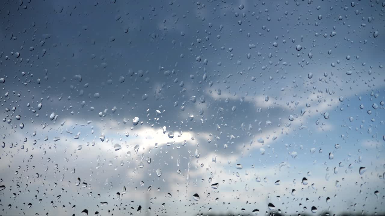구름이 많은 하늘을 향한 비방울을 가진 차의 앞 유리창을 통한 시야. 비가 오는 날 차량의 창문 위에 물방울의 근접.