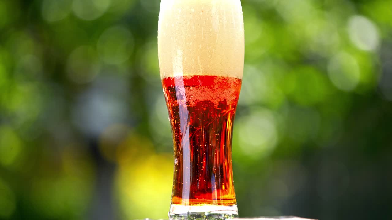 White foam becoming into dark beer with bubbles in glass. Foamy alcohol beverage in a tall glass on blur background. Close-up.