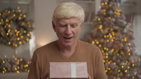 portrait of old happy man holding a christmas present and looking at the camera