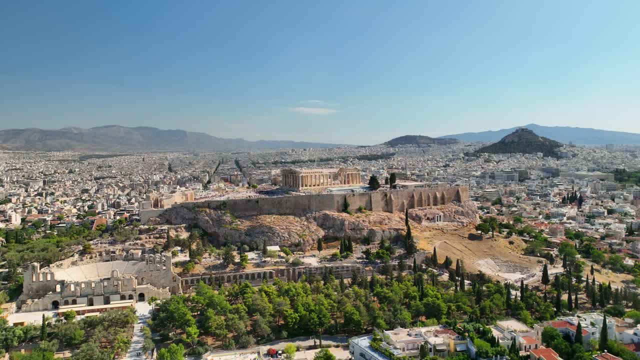 Aerial UHD footage of Acropolis, shot in full daylight, showing ancient columns, theater, and classical architecture with sprawling Athens in the background.