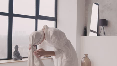 목욕 가운을 입은 여성이 머리를 말리기 위해 수건을 머리에 감습니다.