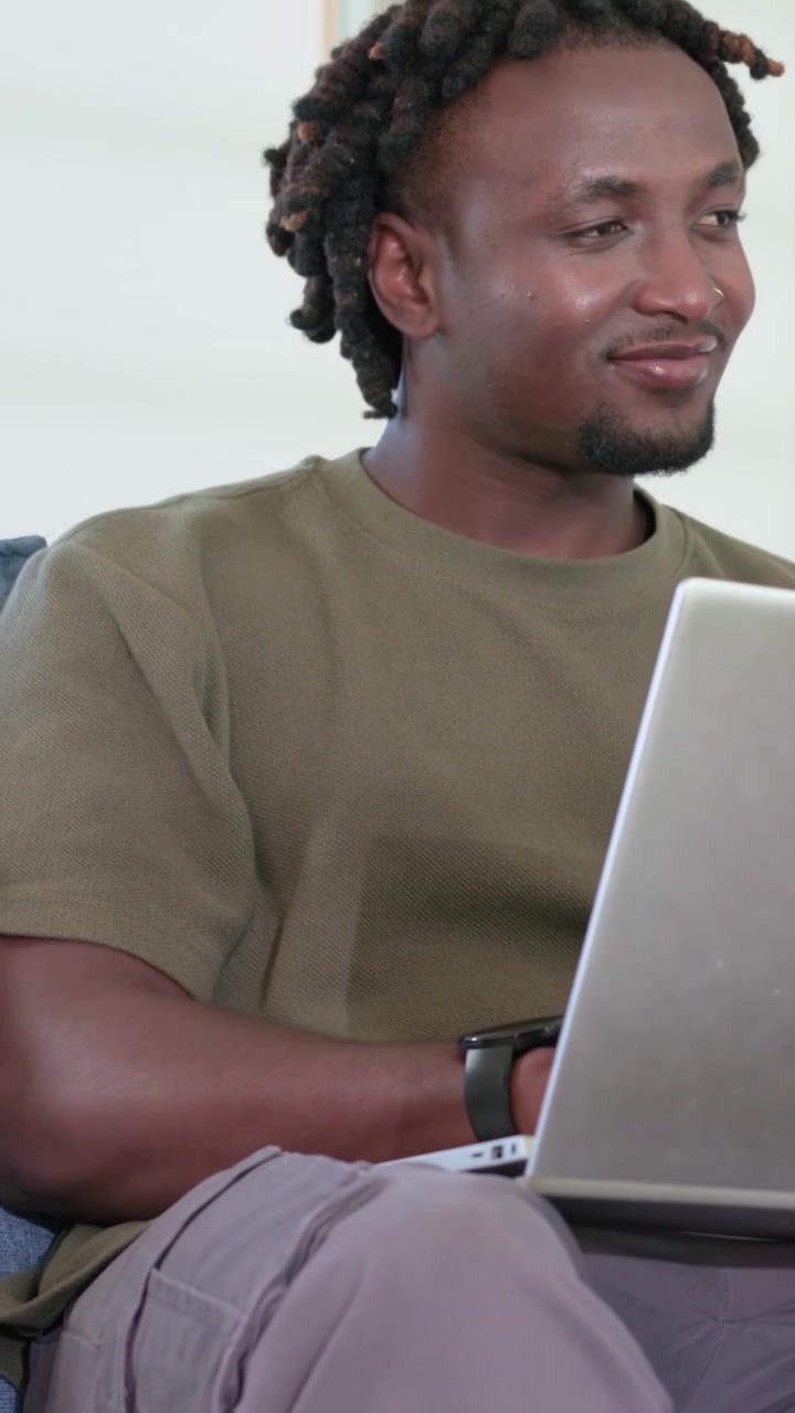 Vertical video: Camera pulling back showing man in olive T-shirt typing on silver laptop to work