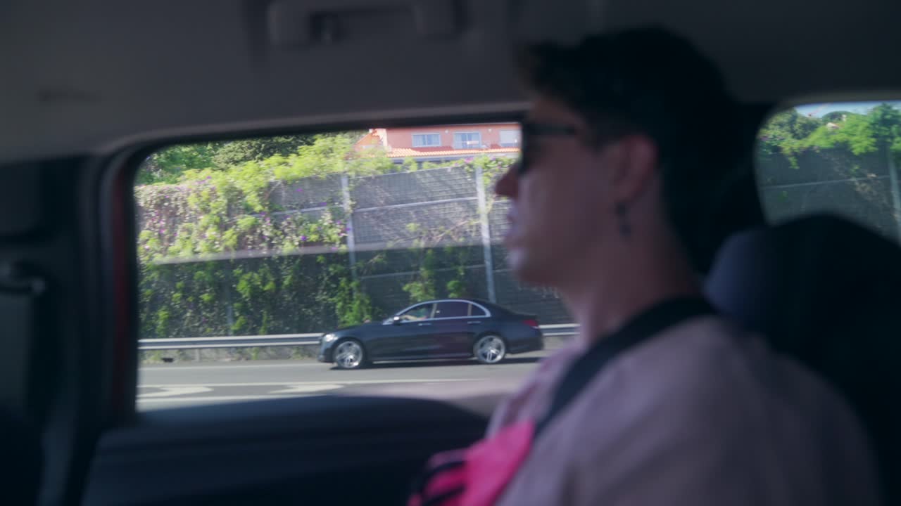 A person looking out of a car window while driving on a highway, with passing vehicles and a sound barrier visible outside