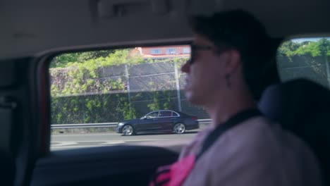 a person looking out of a car window while driving on a highway, with passing vehicles and a sound barrier visible outside