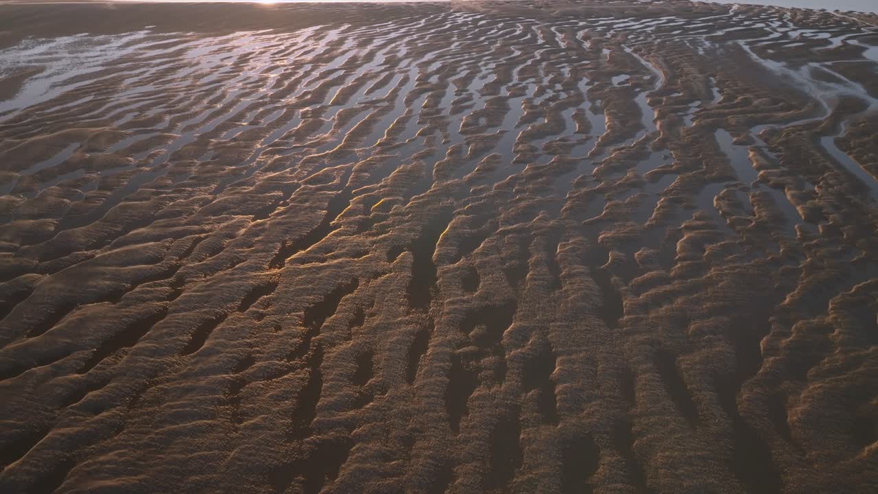Tidal sand patterns and seawater pools at golden hour. Slow flight over with gradual descent.