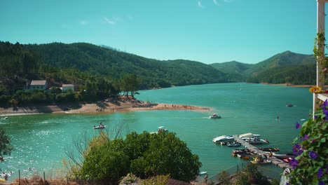 lake pier with sport boats at marina with swimming people, padle practicing among mountain pine trees at sunshine in wide shot 4k