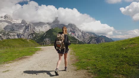 view from behind of a hiker tourist traveler woman with backpack trekking and walking on a mountain path with the dolomites in the background