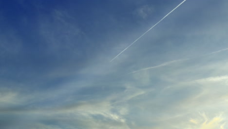 a flying airplane leaves contrails in a beautiful blue sky with clouds during the day