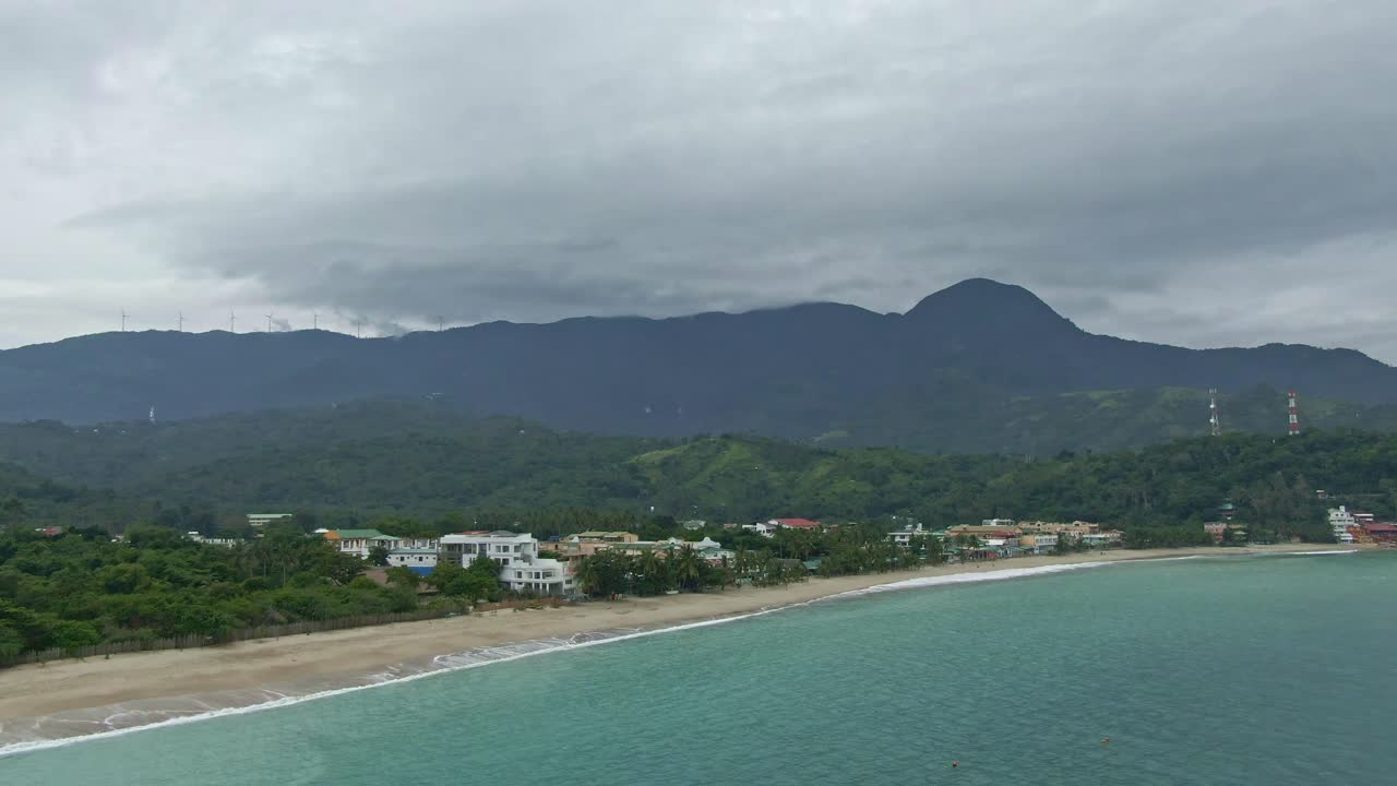 해안선, 하얀 해변, 부서지는 파도, 흐린 날 배경의 산 꼭대기에 있는 풍차, 잔잔한 청록색 물의 아름다운 장면