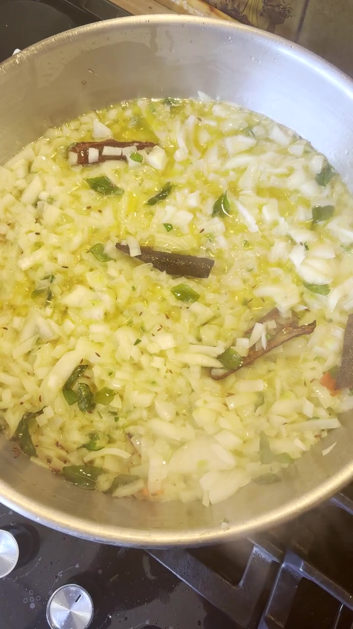 Friggere cipolle bianche e verdi con bastoncini di cannella in padella su fornello a gas. Verticale.