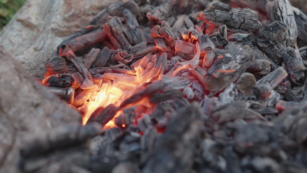 An extreme close-up, static shot of intensely glowing embers and hot charcoal in a campfire. The pulsating heat and bright orange core create a mesmerizing and warm atmosphere.