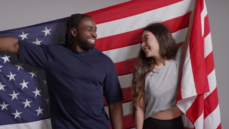 retrato de estudio de una pareja multicultural con una bandera estadounidense detrás de ellos celebrando el 4 de julio, día de la independencia 4
