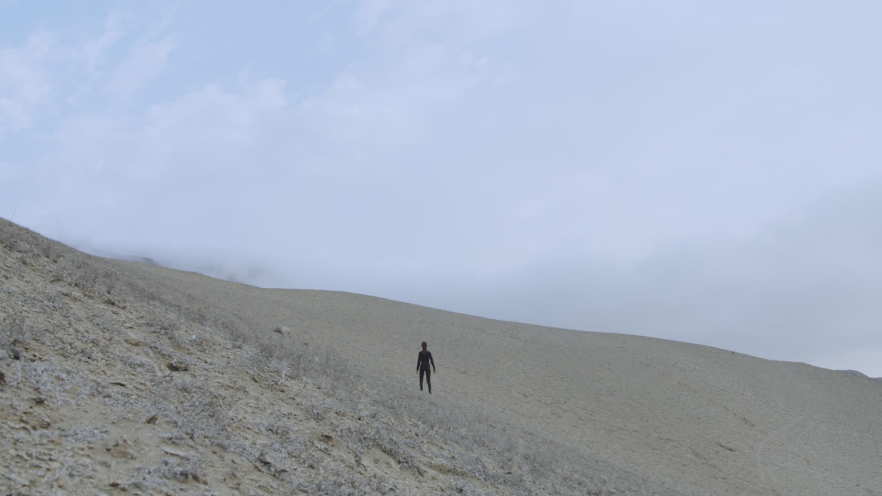 슬로우 모션으로 세게 부는 바람과 함께 아무데도 없는 사막에서 검은 옷을 입은 여자의 큰 와이드 샷