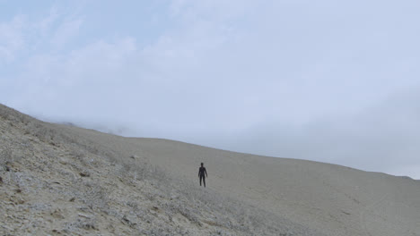 Gran-Plano-General-De-Una-Mujer-Vestida-De-Negro-En-El-Desierto-Mirando-A-Su-Alrededor-En-Medio-De-La-Nada-Con-El-Viento-Soplando-Fuerte-En-Cámara-Lenta