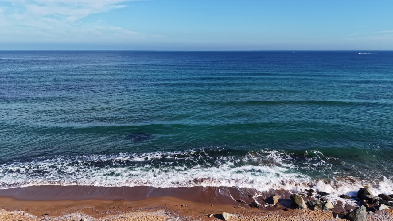 Tranquilla vista sul mare che cattura dolci onde che si infrangono su una spiaggia sabbiosa sotto un cielo azzurro limpido a mezzogiorno.