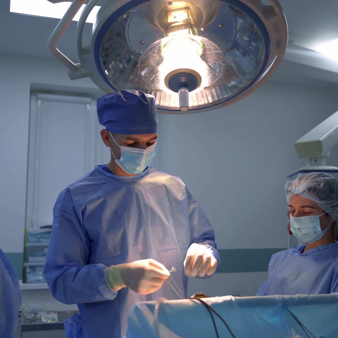Surgeon professional gives the forceps to his assistant. Doctor takes a thread and tries to make a knot. Surgery at backdrop