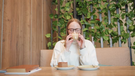 young lady sits in cozy cafe with eyes closed and joyful smile, hands together in gratitude, ready to enjoy chocolate cake and smoothie