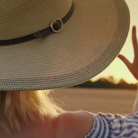 una mujer con un sombrero ancho extiende su mano hacia el sol