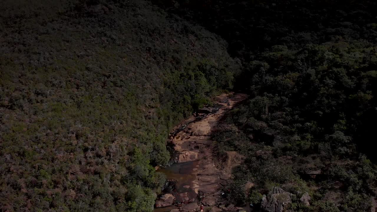Rock plateau river bed with stream of a river cascading and forming ponds. Aerial descend revealing the wider landscape against a blue sky with clouds and steep cliff drop
