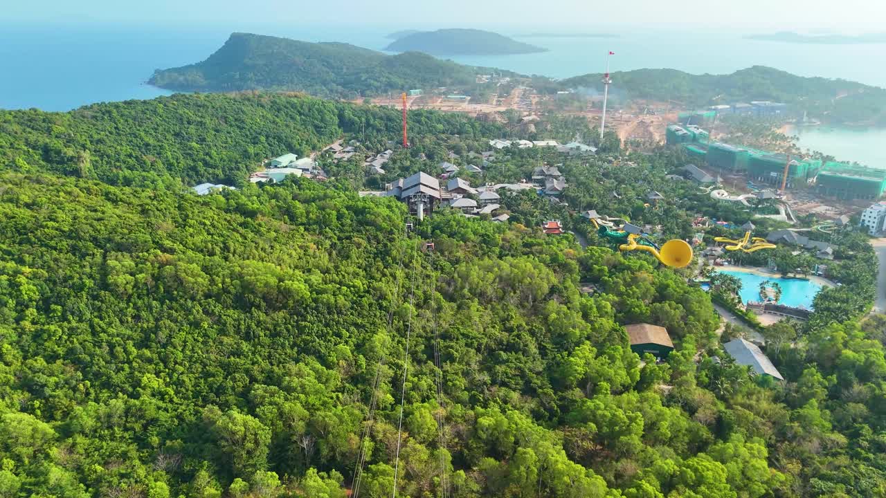 Drone shot of the longest three-rope cable car in Phu Quoc Island, Vietnam, gliding over lush green forests and scenic landscapes, with a panoramic view of the coastline and surrounding mountains.
