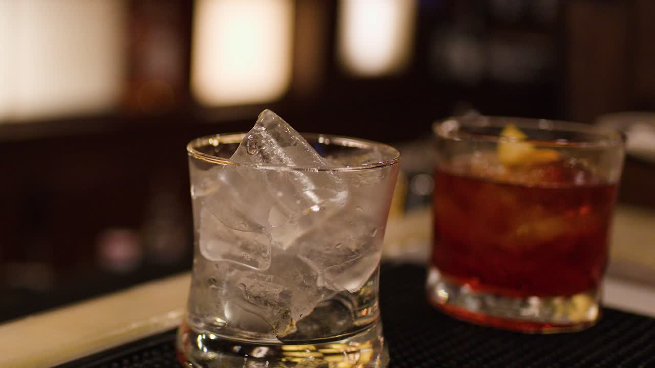 Bartender prepares whiskey cocktail with ice in dimly lit Bangkok bar, shallow depth of field