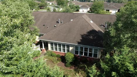 Descending-aerial-between-trees,-push-in-shot-on-rear-back-of-home,-house-with-many-windows-in-American-single-story-modern-housing-development