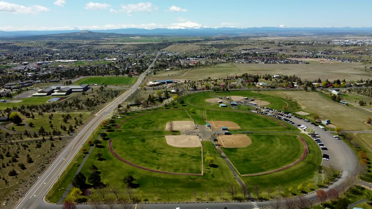 US, Oregon, Madras, Juniper Hill Park, 2025-04-19 - Drone view flying over the Juniper Hill sports complex. With baseball fields, soccer fields, parking, and a view of the city beyond.