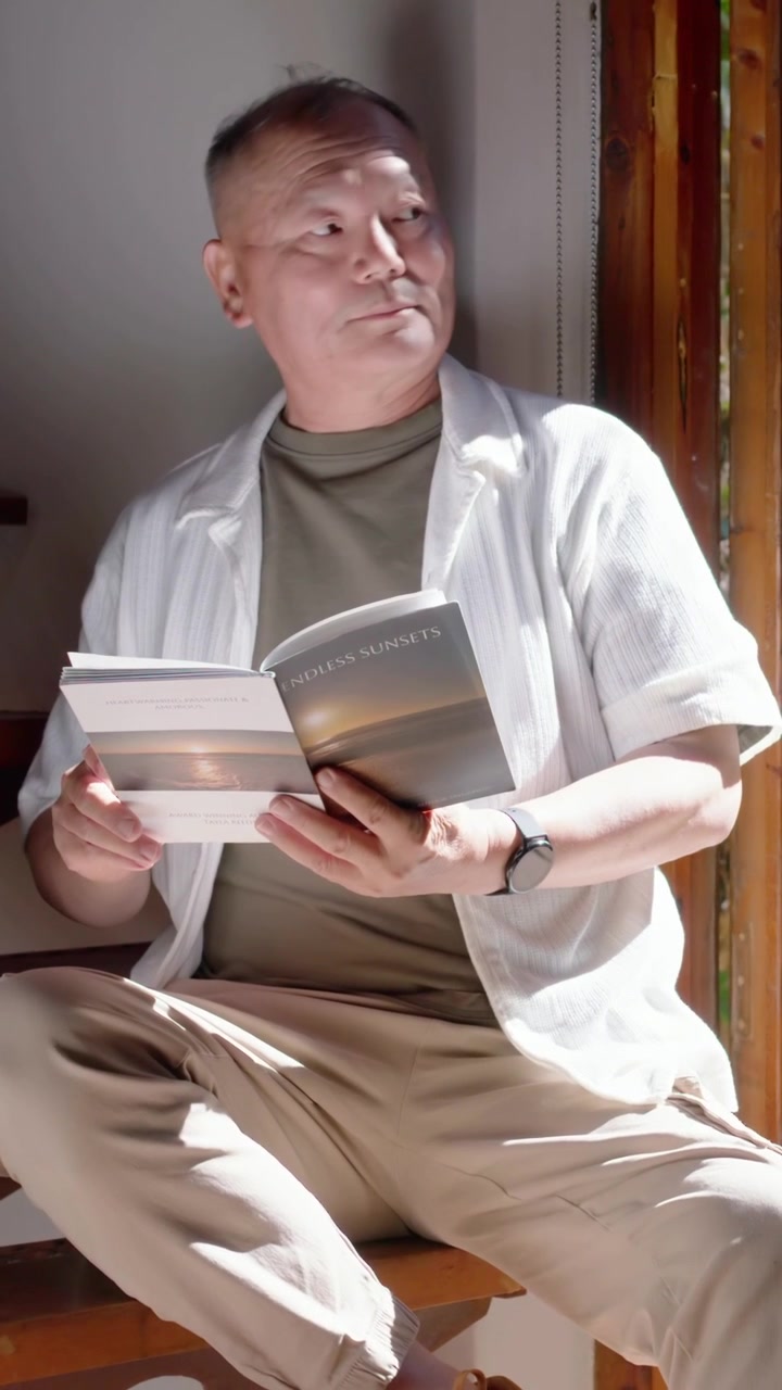 Vertikales Video: Kamera schwenkt zu einem älteren Mann, der am Fenster ein Buch liest, Seiten umblättert und bei einem Geräusch aufblickt.